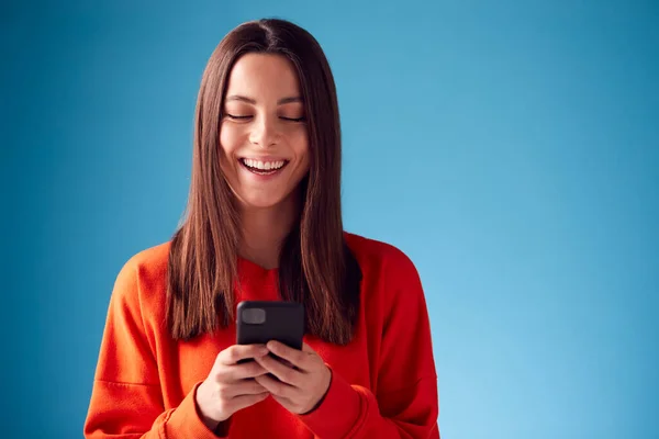 Retrato Estudio Una Joven Sonriente Mirando Teléfono Móvil Contra Fondo — Foto de Stock