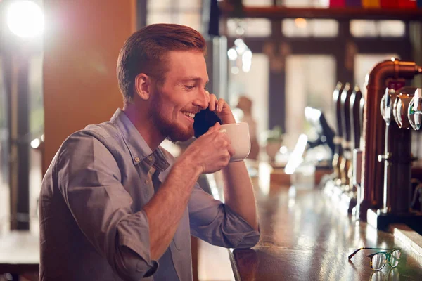 男性オーナーやバーの店長がカウンターでコーヒーを飲みながら携帯電話で話す — ストック写真