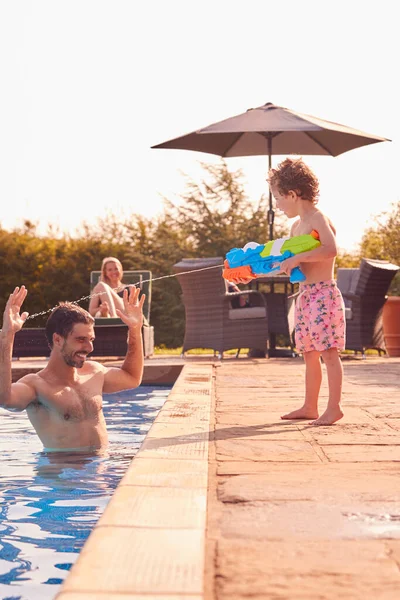 Sohn Spritzt Vater Mit Wasserpistole Schwimmbad Sommerurlaub — Stockfoto