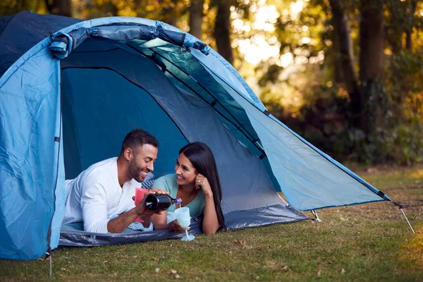 テントで寝そべっているカップルをキャンプシャンパンを飲みながら — ストック写真