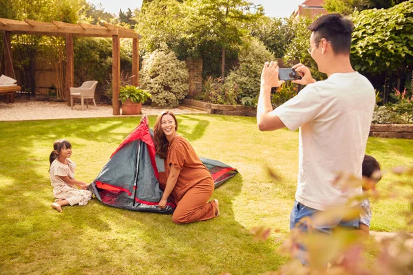 亚洲人的父亲在家里的花园里挂帐篷时 用手机拍照 — 图库照片