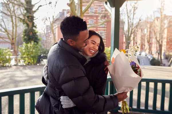 当他们在城市公园相遇时 浪漫的男人在送给年轻女人一束鲜花后拥抱她 — 图库照片