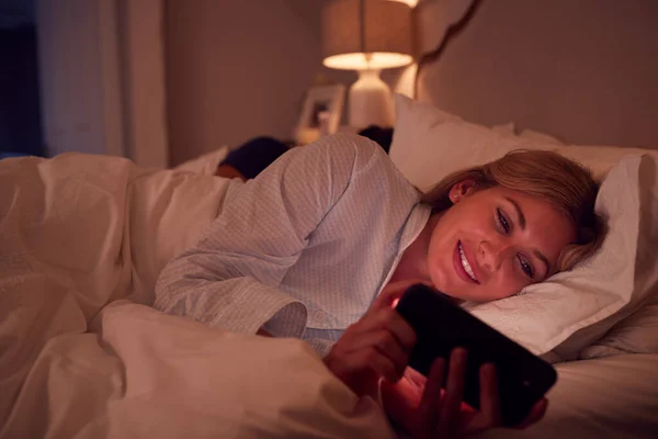 Geceleri Yatakta Uzanan Cep Telefonu Ekranına Bakan Çift — Stok fotoğraf