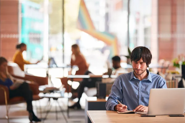 現代のオープンプランオフィスでノートを書いてデスクに座っているビジネスマン — ストック写真