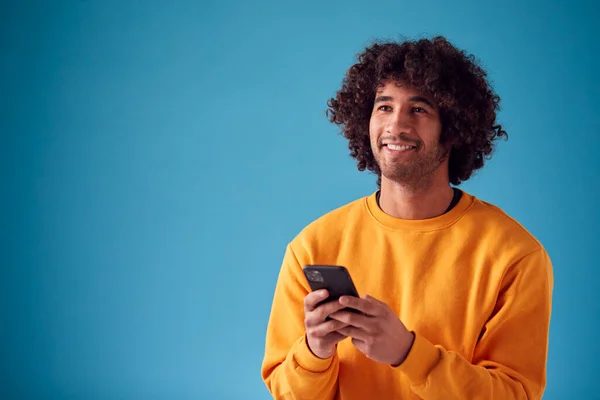 Studio Porträtt Leende Ung Man Tittar Mobiltelefon Mot Blå Bakgrund — Stockfoto