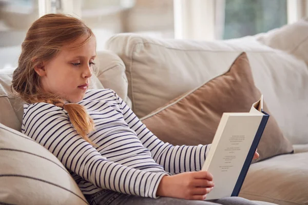 Νεαρό Κορίτσι Χαλαρώνοντας Στον Καναπέ Στο Σπίτι Διαβάζοντας Βιβλίο — Φωτογραφία Αρχείου