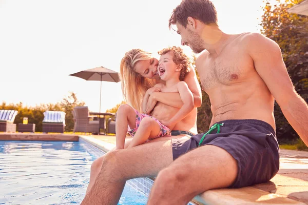 有年幼儿子的家庭坐在游泳池边 在室外游泳池里享受暑假的乐趣 — 图库照片