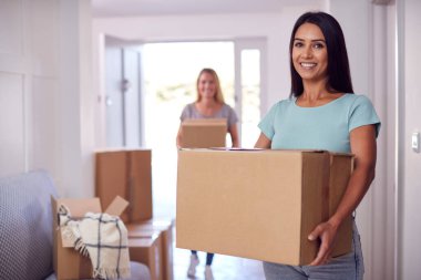 Portrait Of Female Couple Carrying Boxes Through Front Door Of New Home On Moving Day clipart