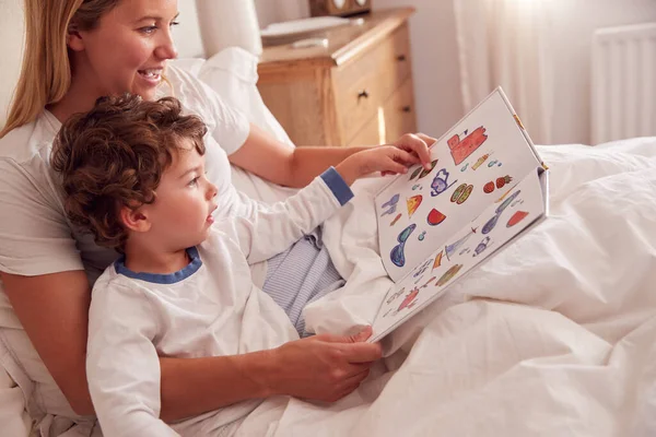 Madre Dormitorio Mirando Libro Fotos Con Hijo Joven Usando Pijamas —  Fotos de Stock