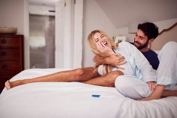 ポジティブ妊娠テストを祝うベッドルームでパジャマを着て興奮したカップル — ストック写真