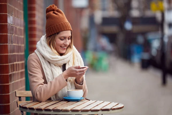 Kobieta Klient Wysyłanie Sms Siedząc Przed Kawiarnią Ruchliwej Ulicy High — Zdjęcie stockowe