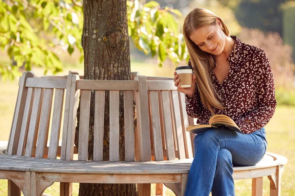 Зрелая Женщина Расслабляется Сидя Скамейке Парке Деревом Чтение Книги Кофе — стоковое фото