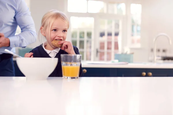 父が仕事の準備をするにつれて キッチンで学校の制服を着て朝食を食べる女の子 — ストック写真