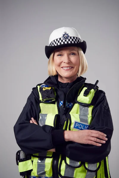 Studio Portrait Of Smiling Mature Female Police Officer Against Plain Background
