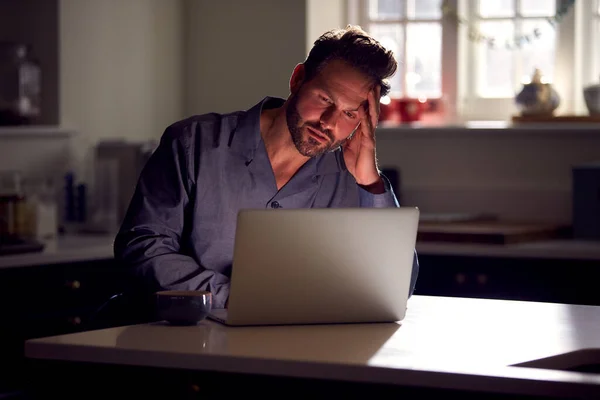 穿着睡衣 穿着不快乐的男人 晚上坐在厨房里用笔记本电脑 — 图库照片