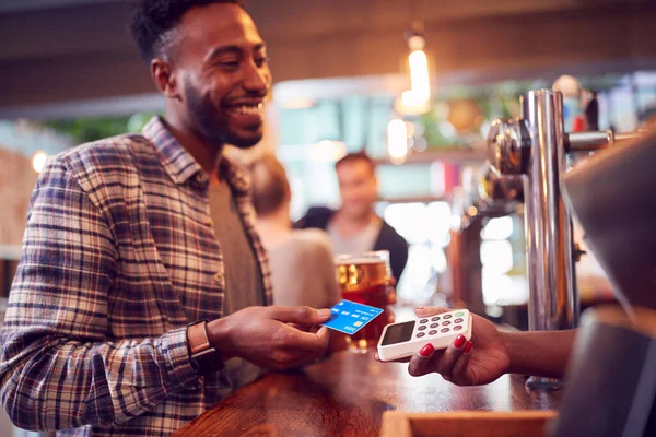 女性のバーテンダーへの飲み物のためのカードで非接触支払を作るバーで笑顔男性顧客 — ストック写真