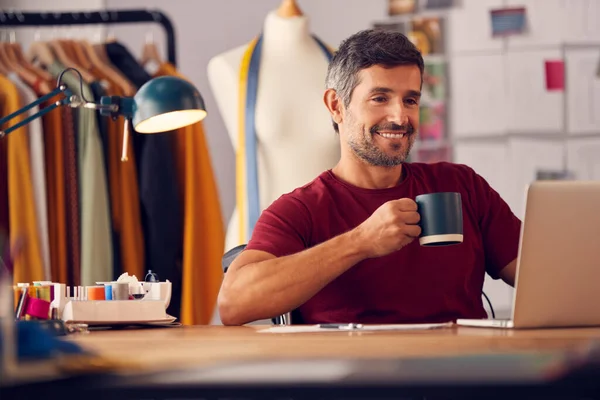 Olgun Erkek Moda Tasarımcısı Stüdyoda Elinde Bir Fincan Kahveyle Dizüstü — Stok fotoğraf