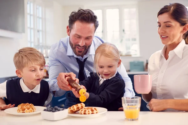 両親が仕事の準備をするにつれてキッチンで学校の制服を身に着けている子供たち朝食ワッフルを食べる — ストック写真