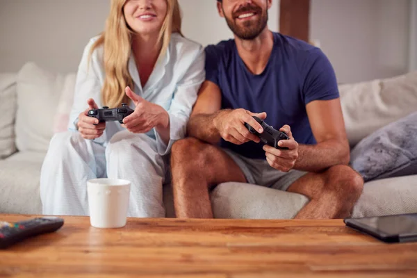 情侣们穿着睡衣坐在沙发上一起玩电脑游戏 — 图库照片