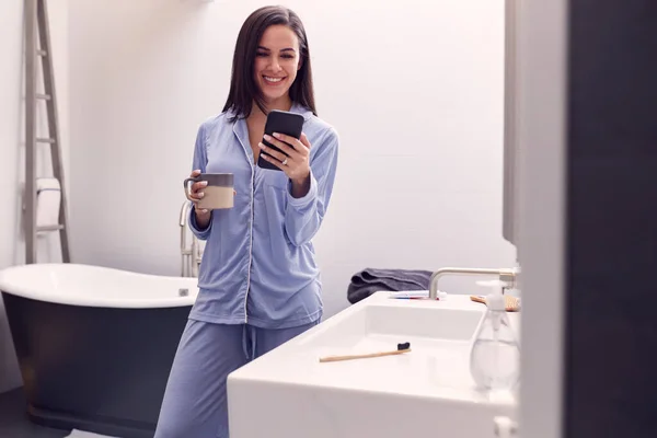 Vrouw Dragen Pyjama Met Warm Drankje Thuis Controleren Mobiele Telefoon — Stockfoto