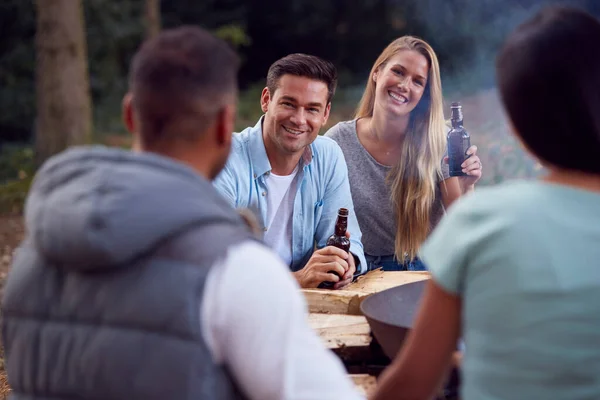 一緒にビールを祝うと飲む火のボウルでたき火で座っている友人のキャンプのグループ — ストック写真