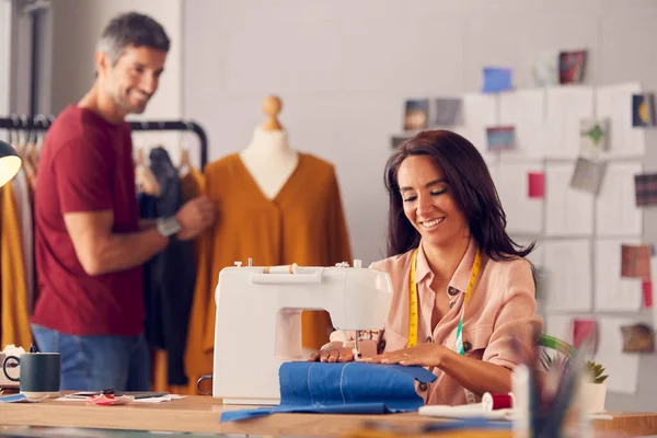 在缝纫机上工作的女性时装设计师作为背景下的男性同事 — 图库照片