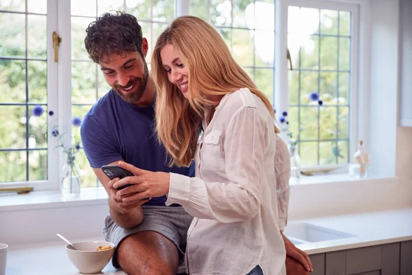 Pareja Usando Pijamas Cocina Usando Teléfono Móvil Mientras Come Desayuno —  Fotos de Stock