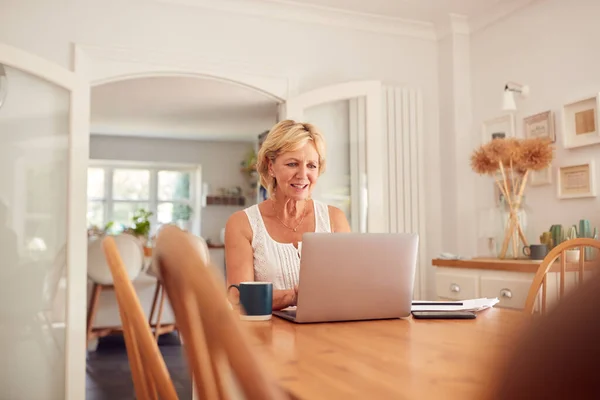 在厨房网上购物的退休妇女和使用笔记本电脑管理家庭财务 — 图库照片