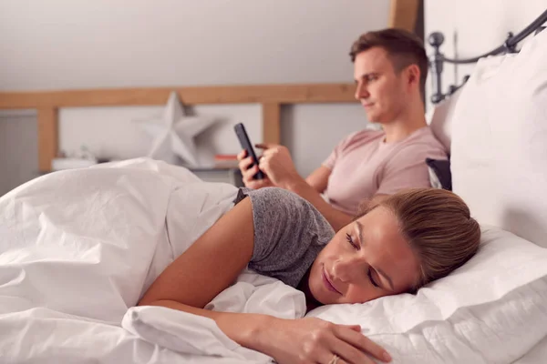 Άντρας Στο Σπίτι Χρησιμοποιώντας Κινητό Τηλέφωνο Στο Κρεβάτι Ενώ Γυναίκα — Φωτογραφία Αρχείου