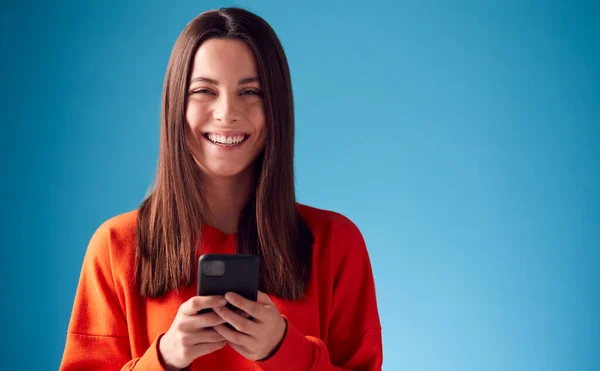 Studio Porträtt Leende Ung Kvinna Tittar Mobiltelefon Mot Blå Bakgrund — Stockfoto