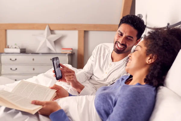 Пара Ліжку Читання Дивлячись Фотографії Мобільному Телефоні Разом — стокове фото