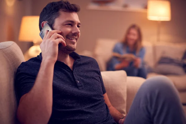 男人谈论手机和阅读女性书籍时 情侣在家里沙发上放松的夜晚镜头 — 图库照片