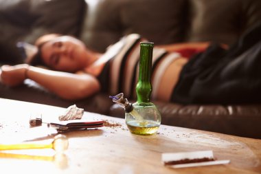 Woman Slumped On Sofa With Drug Paraphernalia In Foreground clipart