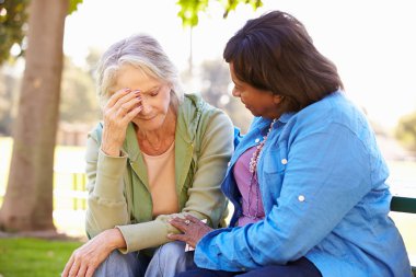 Woman Comforting Unhappy Senior Friend Outdoors clipart