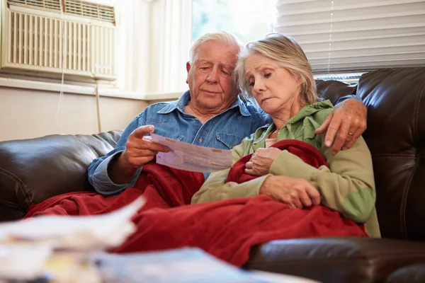 Besorgtes Senioren-Paar sitzt auf Sofa und schaut sich Rechnungen an — Stockfoto