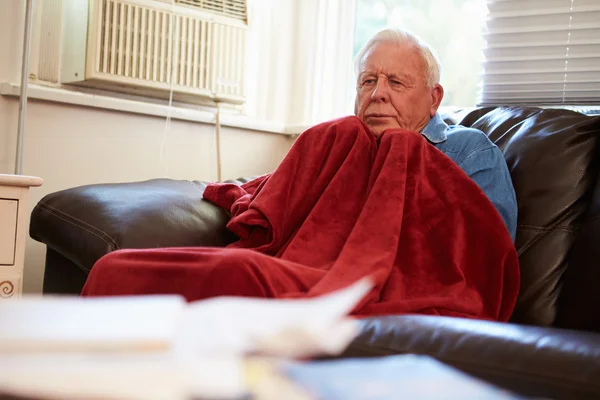 Uomo anziano cercando di mantenere caldo sotto coperta a casa — Foto Stock