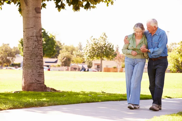 Старший мужчина помогает жене, когда они идут в парк вместе — стоковое фото
