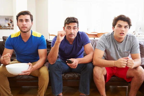 Группа мужчин, сидящих на диване и смотрящих спорт вместе — стоковое фото