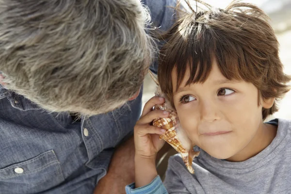 Boy listening to seashell with grandfather — Stock Photo, Image