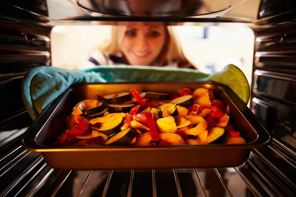 Mujer poniendo verduras en el horno — Foto de Stock