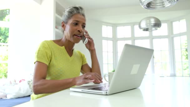 Vrouw met behulp van laptop en praten over telefoon — Stockvideo