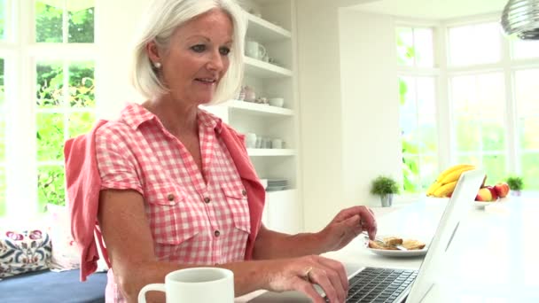 Vrouw met behulp van laptop en eten ontbijt — Stockvideo