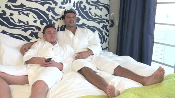Мужская пара в халатах, смотрящая телевизор в номере отеля — стоковое видео