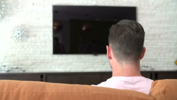 Man zit op Sofa draaien op televisie — Stockvideo