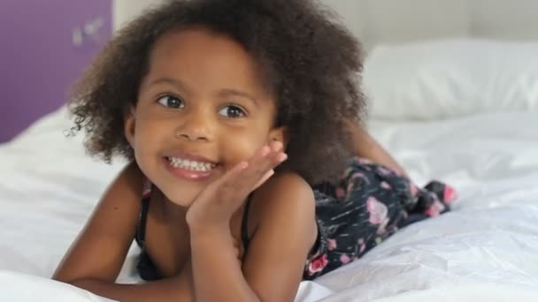 Милая маленькая девочка лежит на животе в кровати родителя — стоковое видео