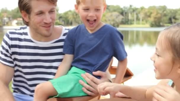 Familia joven sentada en el muelle del lago — Vídeo de stock