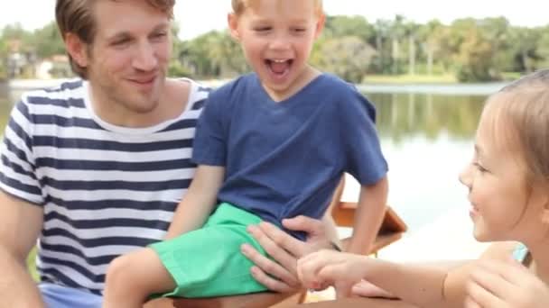 Young family sitting on lake quay — Stock Video