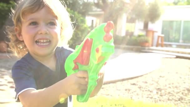 Мальчик размахивает водяным пистолетом в саду — стоковое видео