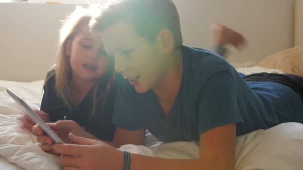 Дети лежат на кровати и с помощью планшета — стоковое видео