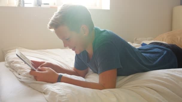 Niño acostado en la cama y usando tableta — Vídeo de stock
